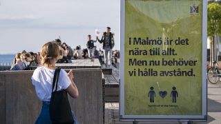 People enjoy the warm evening weather in Malmo, Sweden, Tuesday May 26, 2020 as a sign reads 'In Malmo everything is near. But now we need to keep a distance'.