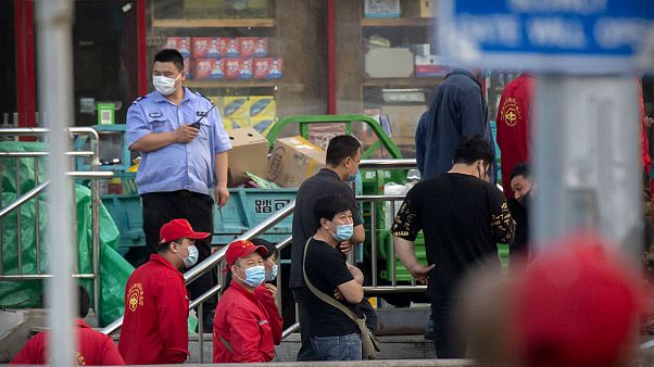Police and security officials watch as workers line up outside a building holding a beef and lamb market in Beijing that was closed by authorities Friday, June 12, 2020 Police and security officials watch as workers line up outside a building holding a beef and lamb market in Beijing that was closed by authorities Friday, June 12, 2020