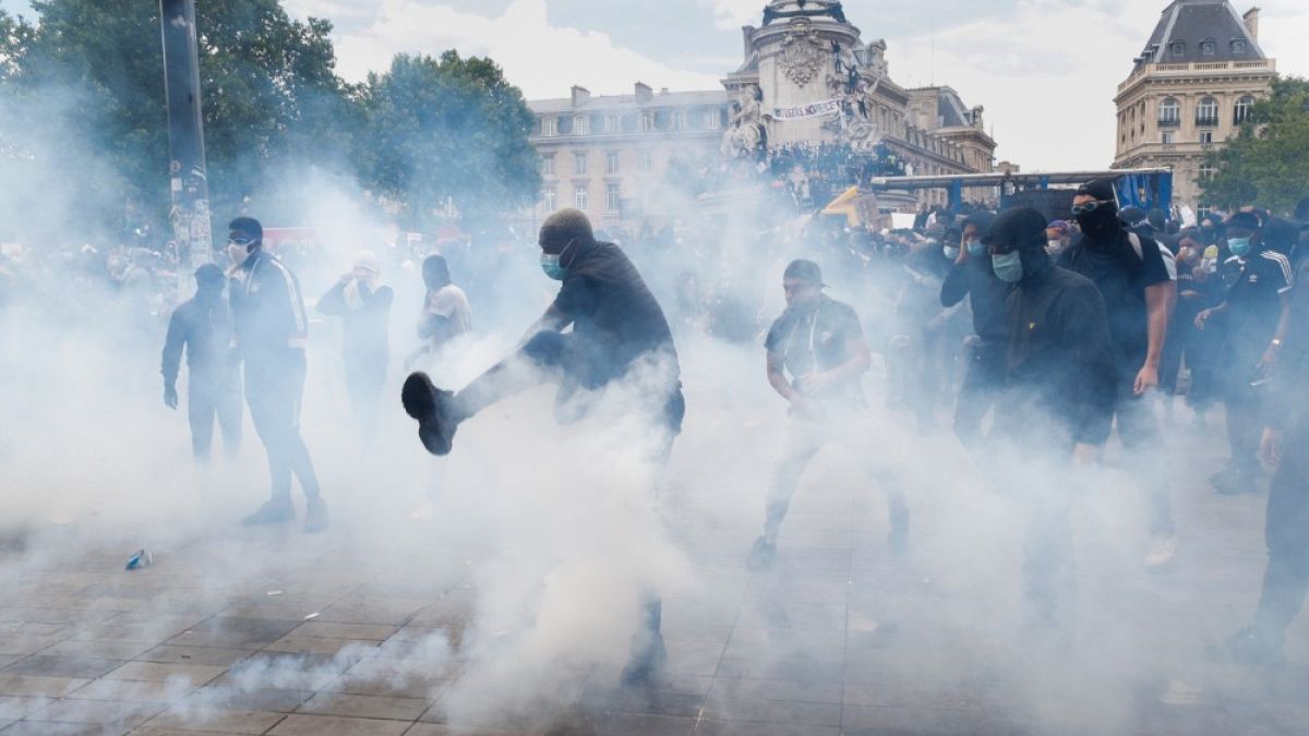 Un uomo dà un calcio a una bomboletta di gas lacrimogeno, durante la marcia contro la brutalità della polizia e il razzismo a Parigi, in Francia