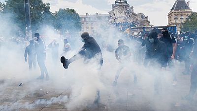Un uomo dà un calcio a una bomboletta di gas lacrimogeno, durante la marcia contro la brutalità della polizia e il razzismo a Parigi, in Francia