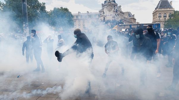 Un uomo dà un calcio a una bomboletta di gas lacrimogeno, durante la marcia contro la brutalità della polizia e il razzismo a Parigi, in Francia Un uomo dà un calcio a una bomboletta di gas lacrimogeno, durante la marcia contro la brutalità della polizia e il razzismo a Parigi, in Francia
