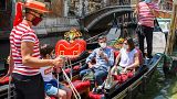 Gondoliers go with customers for a gondola ride on a canal in Venice on June 12, 2020