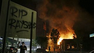 "RIP Rayshard" is spray painted on a sign as as flames engulf a Wendy's restaurant during protests in Atlanta