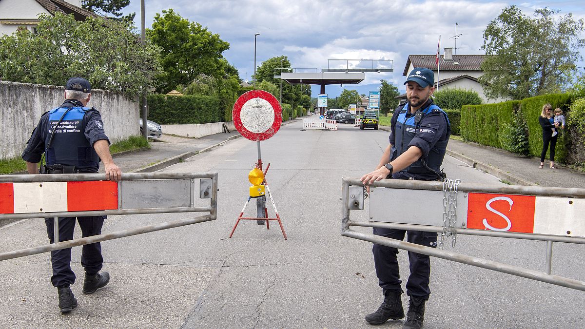 Two border guards opens the barrier that closed access to customs, in Thonex near Geneva, Switzerland, on Sunday, June 14, 2020.