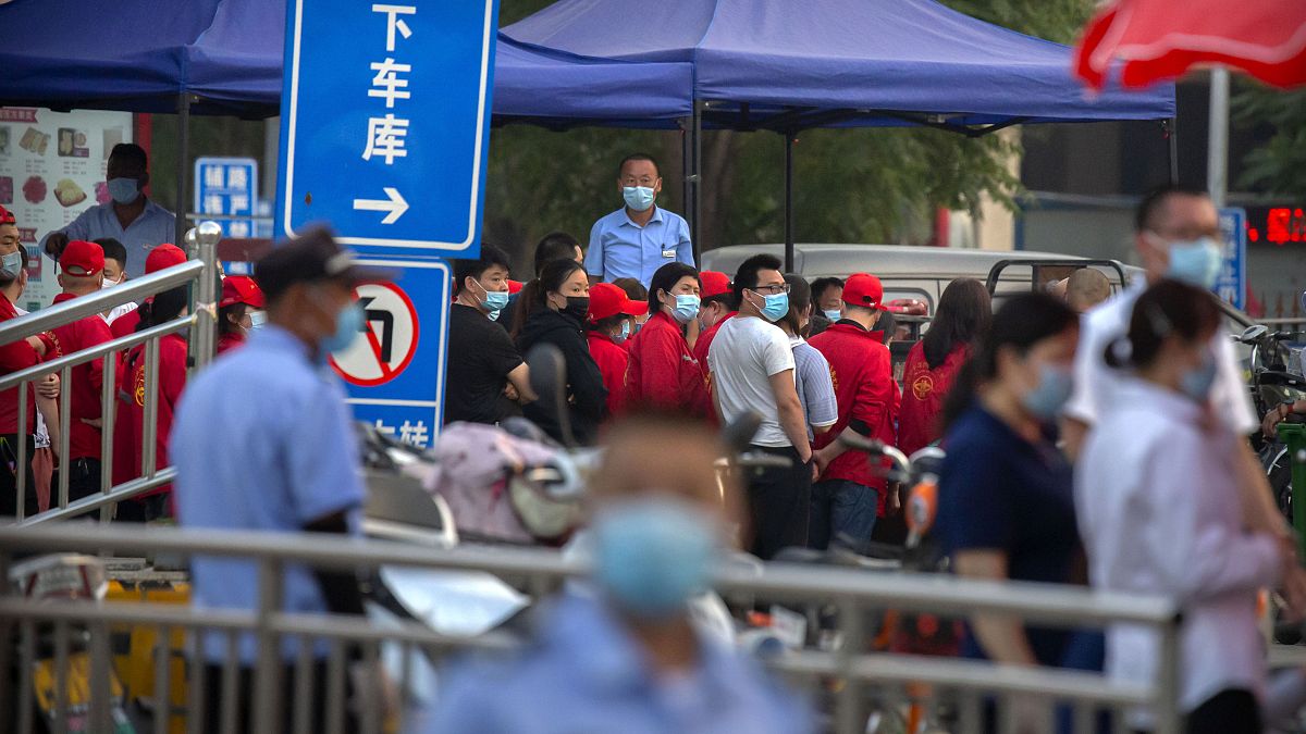 Des agents de sécurité regardent les travailleurs faire la queue devant un bâtiment proche d'un marché qui a été fermé à Pékin, le 12 06 2020