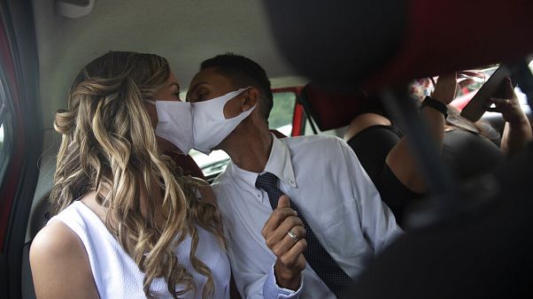 Wearing masks to prevent the spread of the coronavirus, a couple kiss during their drive-thru wedding in Brazil. Wearing masks to prevent the spread of the coronavirus, a couple kiss during their drive-thru wedding in Brazil.