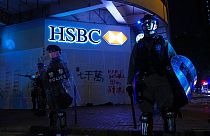 Police stand guard in front of a vandalized HSBC bank