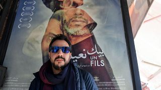 معلقة إشهارية للفيلم التونسي "بيك نعيش" يقف أمامها المخرج مهدي البرصاوي
