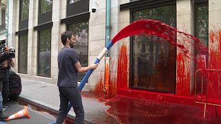 Mid shot activist spraying the Medef headquarters facade with fake blood