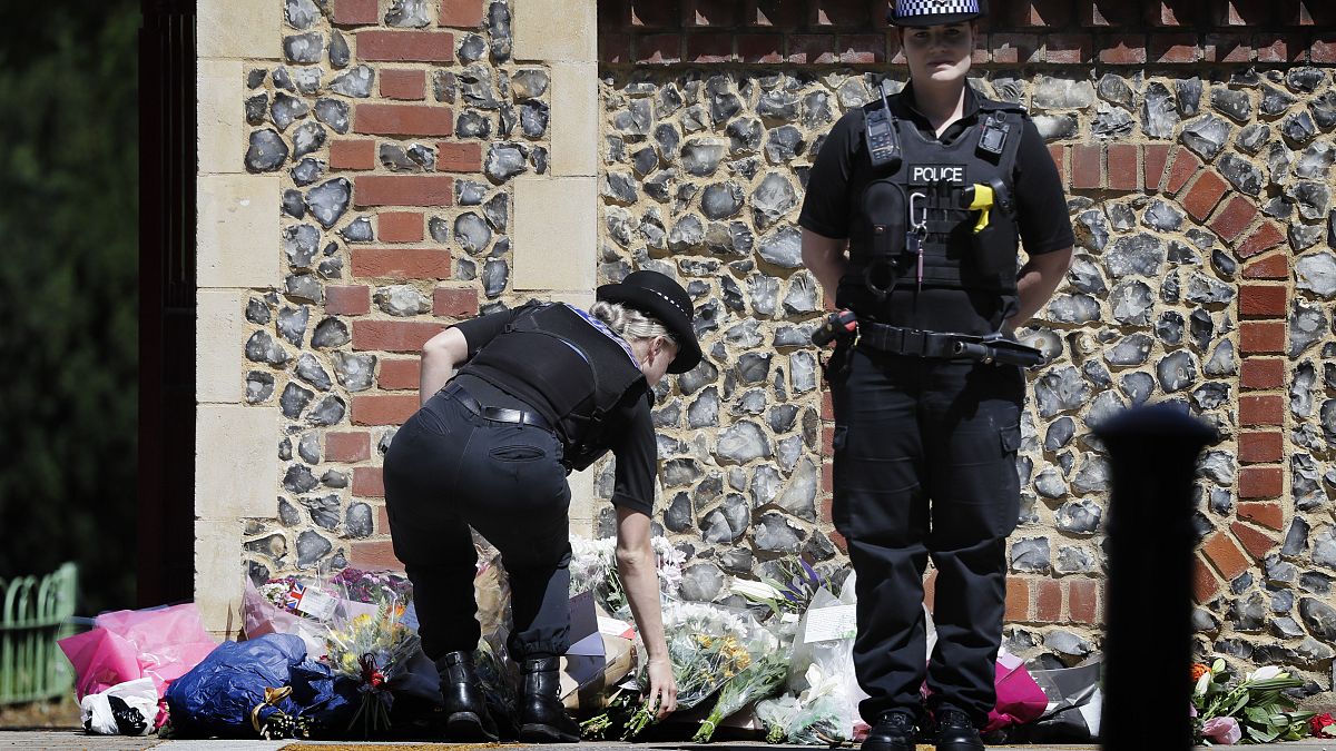 A Police officer places flowers from a woman at the scene of a fatal multiple stabbing attack in Forbury Gardens, central Reading, England, Monday June 22, 2020.