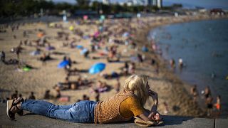 Une femme fume allongée sur un mur alors que les gens profitent de la plage de Barcelone, en Espagne, le dimanche 21 juin 2020.