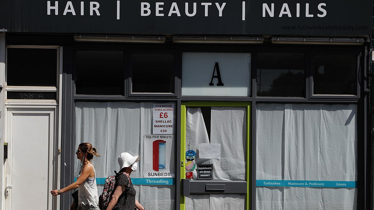 People walk past a closed hair and beauty salon in London, Tuesday, June 23, 2020. 