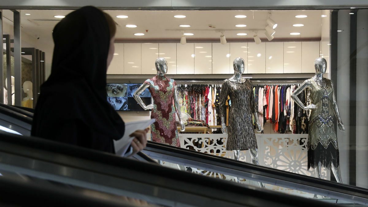 A woman rides an escalator as she looks at a women's dress shop display in a shopping center at Tehran's Grand Bazaar, Iran