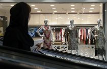 A woman rides an escalator as she looks at a women's dress shop display in a shopping center at Tehran's Grand Bazaar, Iran