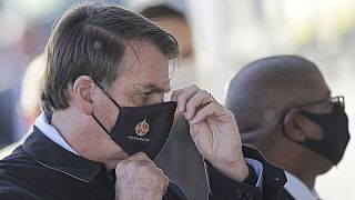 Brazil's President Jair Bolsonaro adjusts his face mask as he speaks to supporters while departing his official residence, Alvorada palace, in Brasilia, Brazil, Thursday, May