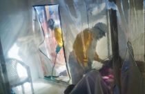 FILE - In this July 13, 2019 file photo, health workers wearing protective suits tend to an Ebola victim kept in an isolation cube in Beni, Congo.