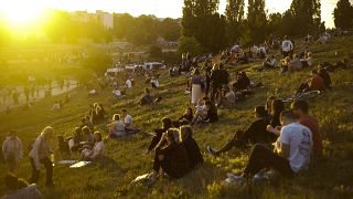 Persone sedute all'aperto mentre il sole tramonta durante il Solstizio d'Estate, nel parco pubblico Mauerpark di Berlino, Germania