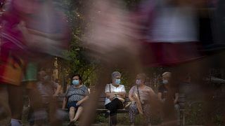 Pedestrians walk past people sit in a bench in Barcelona, Spain, Sunday, June 21, 2020.