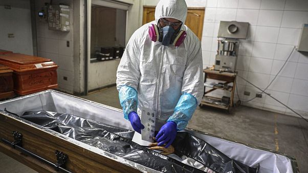 In this Saturday, June 27, 2020 file photo an employee takes the fingerprints of a woman who died from coronavirus, in Santiago, Chile. In this Saturday, June 27, 2020 file photo an employee takes the fingerprints of a woman who died from coronavirus, in Santiago, Chile.