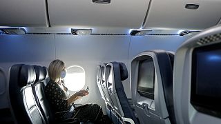 A woman uses a sanitising wipe while setting into her seat on a flight in the US
