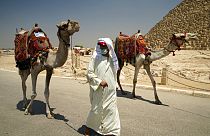A camel guide wears a surgical mask while pulling his camel at the Giza Pyramids in Giza, Egypt