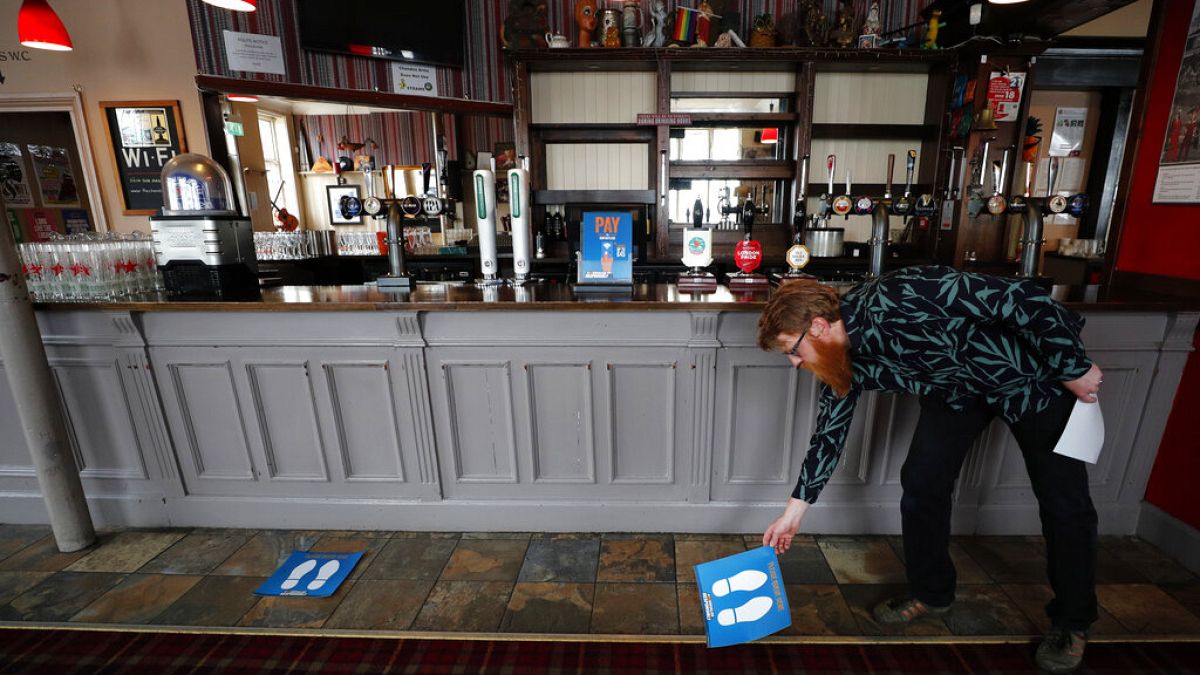Owner Are Kjetil Kolltveit from Norway places markers for social distancing on the front of the bar at the Chandos Arms pub in London, Wednesday, July 1, 2020.