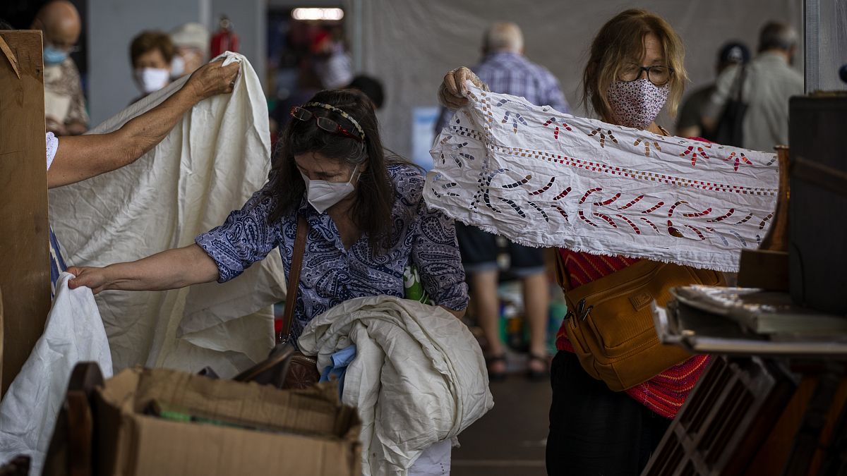 Customers wearing face masks pick second hand fabrics in a market in Barcelona on Wednesday, July 8, 2020.