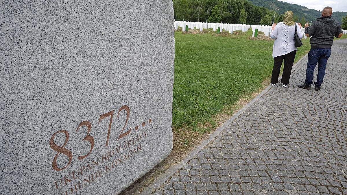 Visitors pray at the memorial cemetery in Potocari, near Srebrenica, Bosnia, Tuesday, July 7, 2020. Writing on stone translates "8372 victims, number is not final'. 