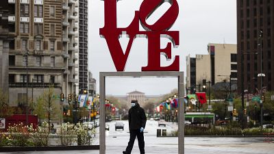 A person wearing a protective face mask and gloves as a precaution against the coronavirus walks by the Robert Indiana sculpture "LOVE" at John F. Kennedy Plaza,