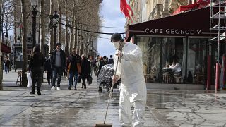 A masked worker wipes the pavement of the Champs Elysees avenue in Paris, Friday, March 13, 2020.