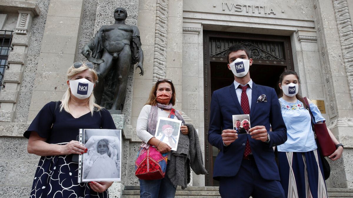 Members of Noi Denunceremo (We will denounce) Facebook group, holds pictures of their relatives, victims of COVID-19, as they stand in front of Bergamo's court.