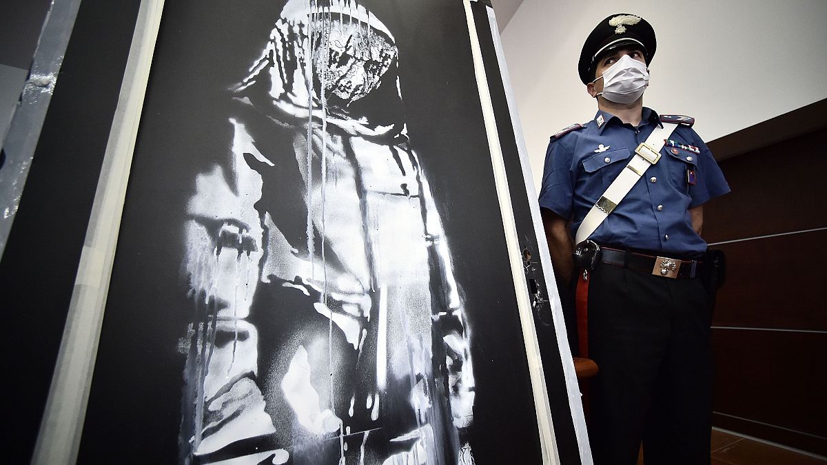 A policeman stands guard near a piece of art attributed to Banksy, that was stolen at the Bataclan in Paris in 2019