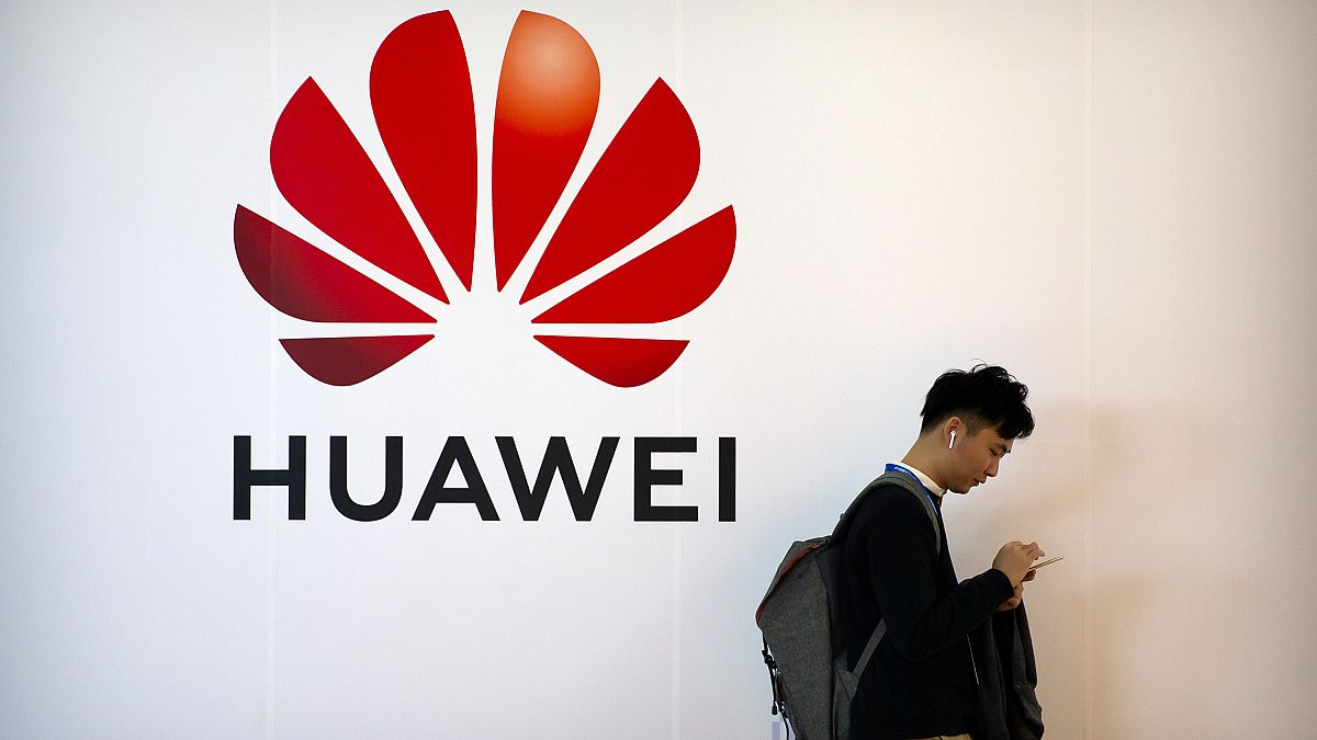 FILE - In this Oct. 31, 2019, file photo, a man uses his smartphone as he stands near a billboard for Chinese technology firm Huawei at the PT Expo in Beijing.