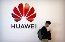 FILE - In this Oct. 31, 2019, file photo, a man uses his smartphone as he stands near a billboard for Chinese technology firm Huawei at the PT Expo in Beijing.