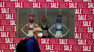 A man wearing a protective face mask walks past a shop window in London