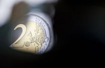 A man takes a photograph of a banner showing a two Euro coin during the presentation of a special edition of the coin at the chancellery in Berlin, Germany, Thursday, Feb. 9,