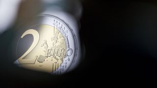 A man takes a photograph of a banner showing a two Euro coin during the presentation of a special edition of the coin at the chancellery in Berlin, Germany, Thursday, Feb. 9, 