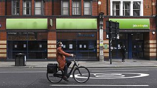 A woman wearing a mask rides a bicycle past a job centre in Shepherd's Bush, London.