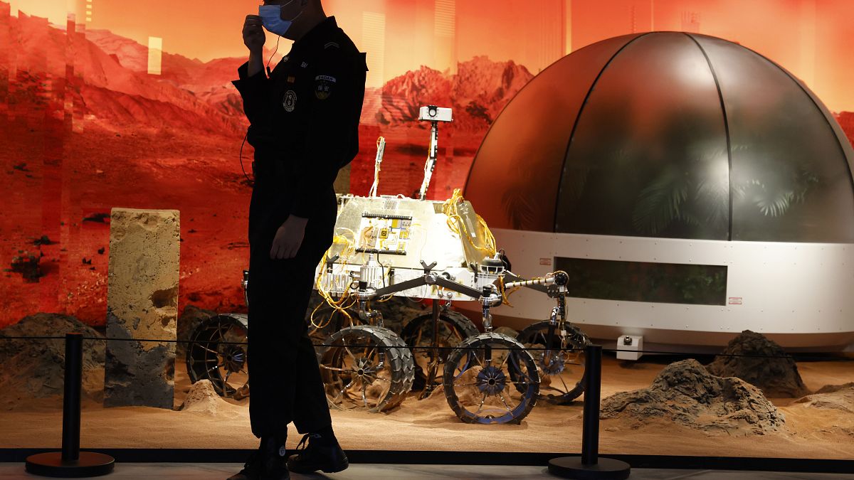 A security guard adjusts his mask near an exhibition of rovers and bio-domes on Mars in Beijing Thursday, July 23, 2020. 