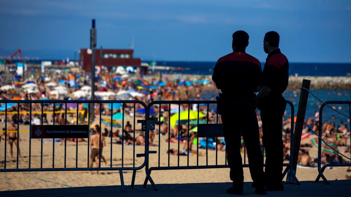 Police officers guard a barrier to stop people entering the beach, in Barcelona, Spain, Saturday, July 18, 2020. 