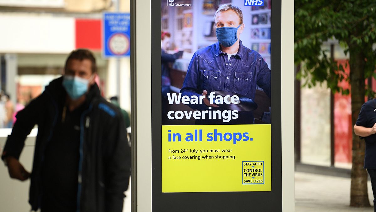 Un hombre con mascarilla en Leeds, ante un cartel anunciando que será obligatoria en comercios