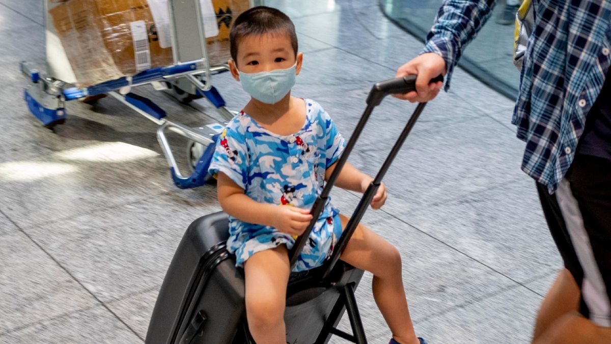 A small boy wearing a mask sits on a suitcase at the airport in Frankfurt, Germany. July 24, 2020.