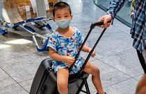 A small boy wearing a mask sits on a suitcase at the airport in Frankfurt, Germany. July 24, 2020.