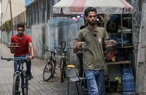 شعبان حمودة (يمين) حاملاً فنجانيْ قهوة بينما يتحضر أحد موظفيه إلى الانطلاق على دراجته الهوائية لخدمة زبائن 