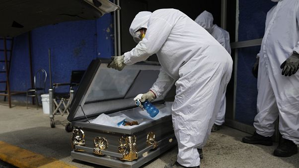 عامل من الجهاز الطبي يرشّ مطهراً داخل تابوت رجل توفي بعد إصابته بكوفيد-19 عامل من الجهاز الطبي يرشّ مطهراً داخل تابوت رجل توفي بعد إصابته بكوفيد-19