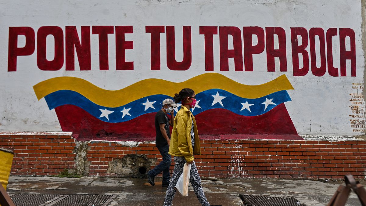 Venezolanos caminan en Caracas ante un cartel que invita a ponerse la mascarilla