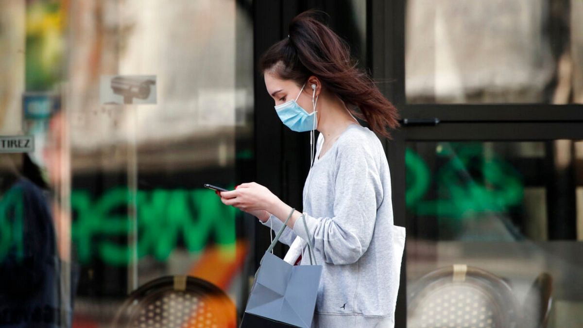 A woman wearing protective face mask looks at her phone past a closed restaurant during a nationwide coronavirus lockdown in Paris, April 20, 2020