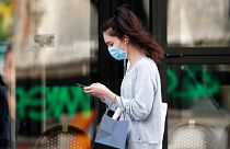 A woman wearing protective face mask looks at her phone past a closed restaurant during a nationwide coronavirus lockdown in Paris, April 20, 2020