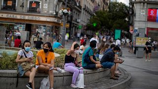 People wearing face masks to prevent the spread of coronavirus, sit on a bench street in downtown Madrid, Spain, Tuesday, July 28, 2020. 