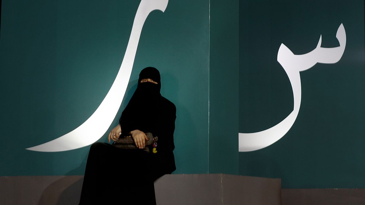 مرأة تجلس عند لافتة مكتوبة بحروف عربية خلال حدث ثقافي  حديقة الواجهة المائية بجدة/ المملكة العربية السعودية